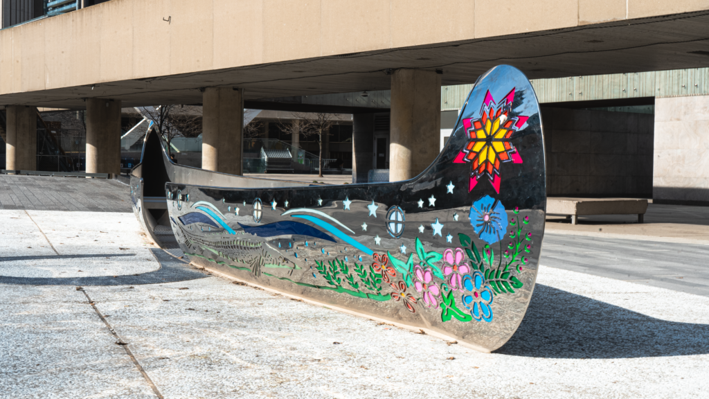 A striking metal sculpture resembling a canoe, positioned on a sidewalk, enhancing the public space with its artistic presence.