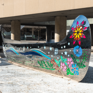 A striking metal sculpture resembling a canoe, positioned on a sidewalk, enhancing the public space with its artistic presence.