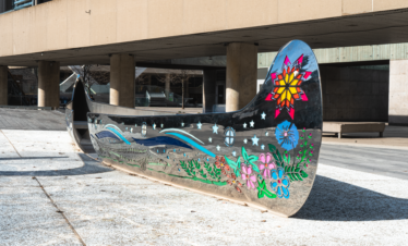 A striking metal sculpture resembling a canoe, positioned on a sidewalk, enhancing the public space with its artistic presence.