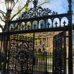 The elegant iron gates, adorned with decorative patterns, stand open, offering a view of the stately building in the background, under the glow of street lamps.