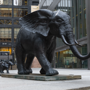 In the middle of the bustling city, the powerful bronze elephant and its smaller companion create a striking contrast against the surrounding glass buildings.