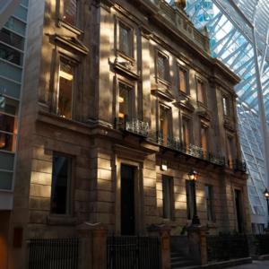 The old-world charm of the building contrasts with the sleek, transparent roof overhead, as sunlight spills over its stone facade and the polished floor below.